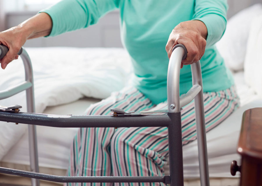 an elderly woman uses a walker to get out of bed
